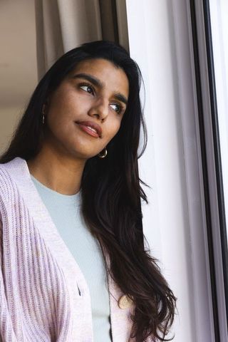 Thoughtful asian woman in pastel cardigan by window at home