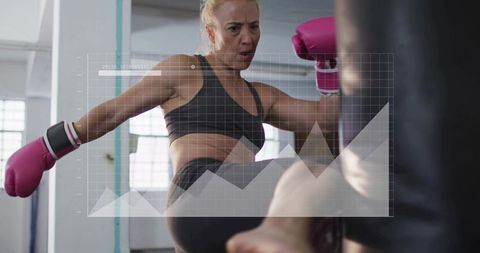 Female boxer kicking heavy bag wearing pink gloves intense gym training