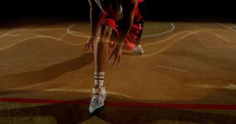 Reaching basketball player stretching on hardwood court in dramatic low-angle spotlight
