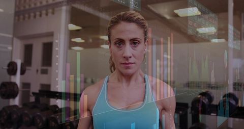 Focused mid-adult woman standing in gym with digital fitness metrics overlay