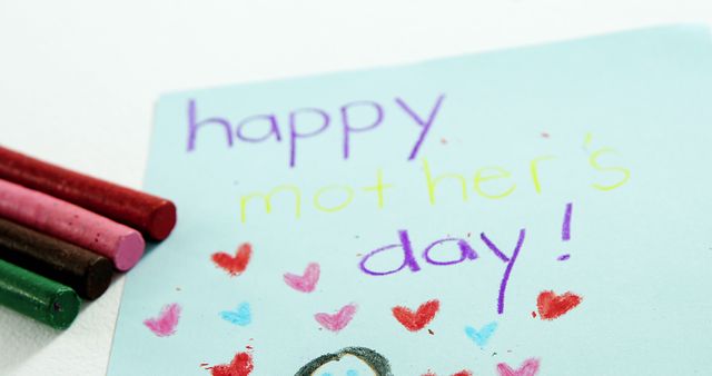 A colorful Mother's Day greeting card created by a child, with crayons lying beside it, with copy space. Handmade cards like this express love and appreciation on special occasions.