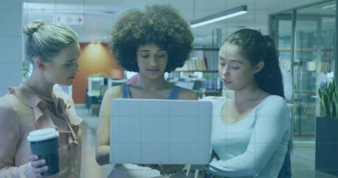 Three colleagues collaborating around laptop in modern open-plan office, teamwork concept