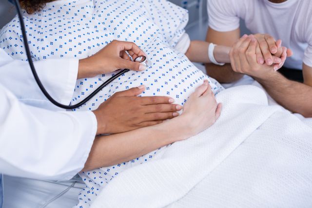 Doctor examining pregnant womans belly with stethoscope in ward of hospital