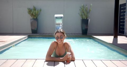 Smiling Woman Relaxing in Swimming Pool with Beverage on Sunny Day