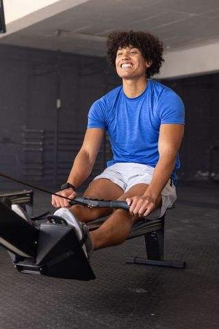 African american man smiling while rowing on gym ergometer in blue activewear