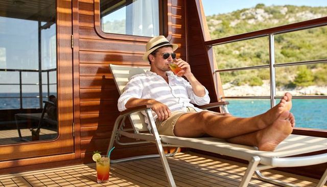 Relaxing man reclining on yacht deck sipping cocktail with scenic coastal view