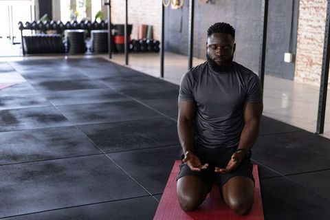African american athlete kneeling on red mat meditating and focusing before workout
