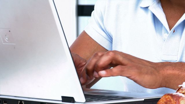 Man engrossed in work on a laptop while enjoying breakfast. Can be used to illustrate productivity, work-life balance, remote work, or morning routine concepts.