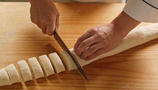 Chef hands cutting rolled dough with knife on wooden board for artisan bread making