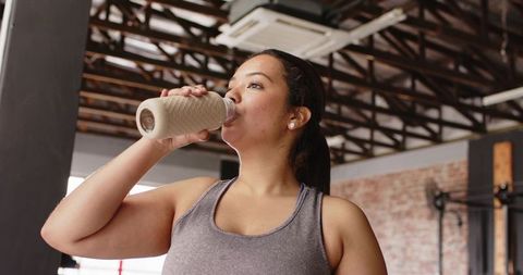 Woman drinking from reusable bottle after workout in industrial gym studio