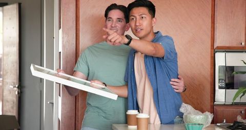Diverse couple unpacking picture frame and coffee in new home kitchen