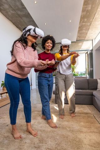 Multicultural women exploring virtual reality together wearing white vr headsets and holding tablet