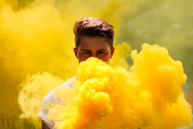 Young man emerging from thick yellow smoke cloud, creating a lively and dynamic atmosphere. Perfect for use in advertising campaigns, festival promotions, artistic or lifestyle content, and social media visuals to convey a sense of fun and celebration.