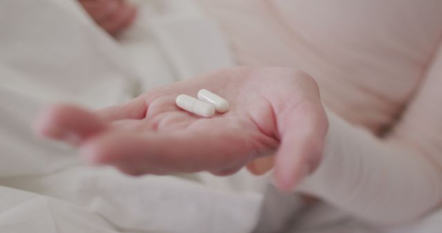 Hand holding white pills over bed - Download Free Stock Images Pikwizard.com