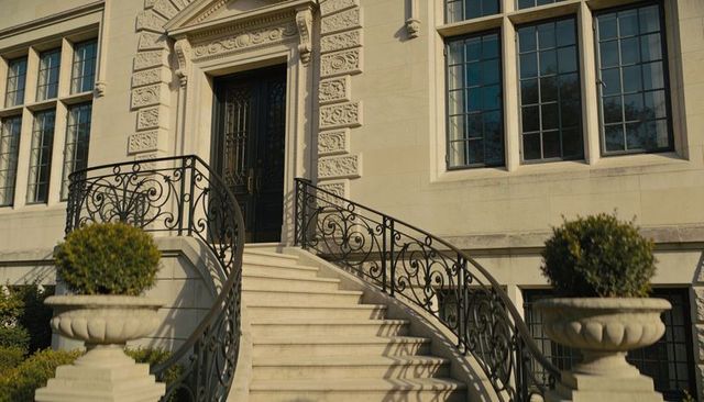 Grand curved limestone staircase with ornate wrought-iron railings leading to double door