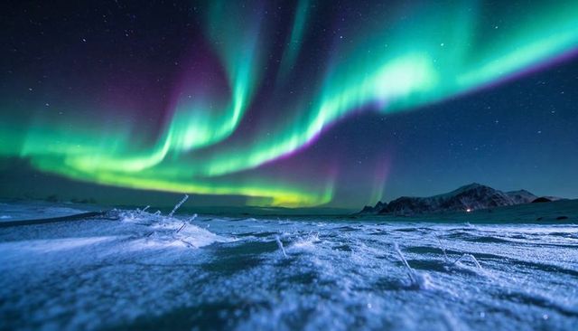 Aurora Borealis Dancing Over Arctic Snowfield With Ice Crystals and Distant Mountains