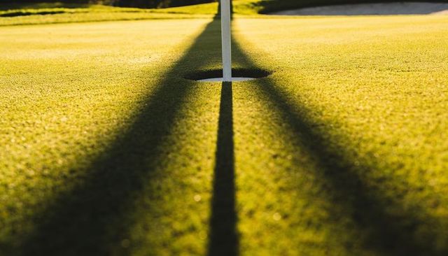 Golden hour flagstick casting long parallel shadows across putting green, cup in focus