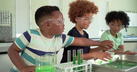 African american boys conducting chemistry experiment with green liquids in classroom lab