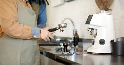 Female barista holding portafilter preparing espresso with grinder and tamper