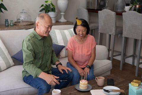 Asian senior couple celebrating cozy at-home birthday with cake, candles and gifts