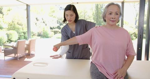 Senior asian woman doing arm exercise with physiotherapist at home