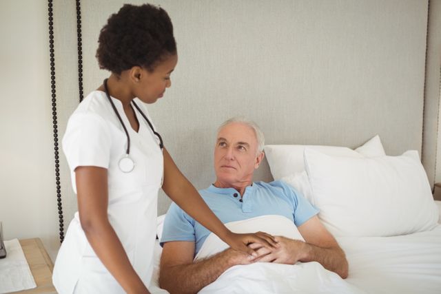 Nurse interacting with senior man on bed at bedroom
