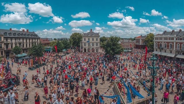 Crowd filling historic town square for summer celebration waving flags and wearing red