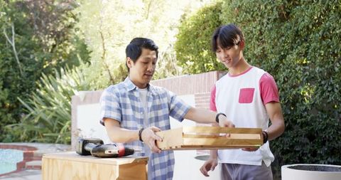 Father and Son Assembling Wooden Drawer Together Outdoors