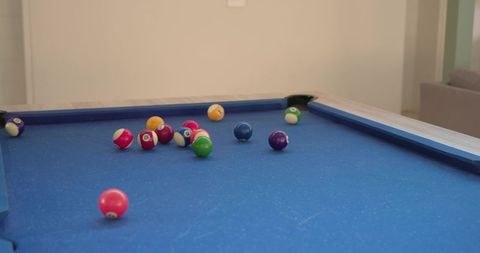 Blue-felt pool table with scattered billiard balls and pockets in modern game room lounge