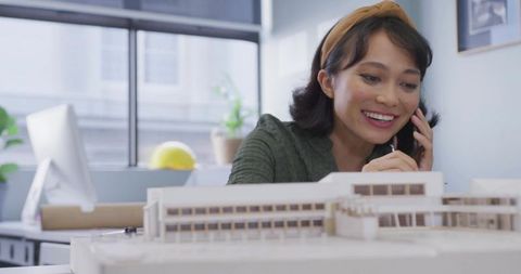 Asian architect woman on phone reviewing scale model in modern design studio