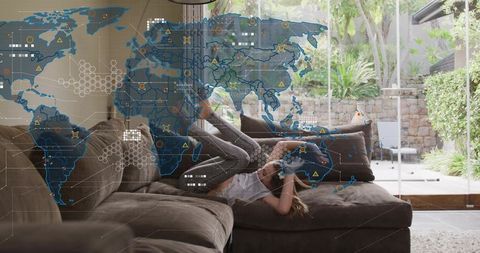 Reclining girl on l-shaped sofa using smartphone with translucent global map overlay