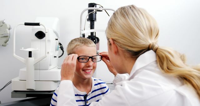 Optician adjusting glasses on happy boy wearing striped shirt at eye clinic focusing on girlfriend's children. Ideal for articles or campaigns about pediatric eye care, optometry, first time visiting eye clinics or children's health checkups.