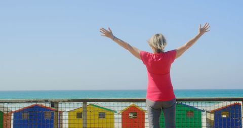 Senior Woman Embracing Beach View by Colorful Beach Huts