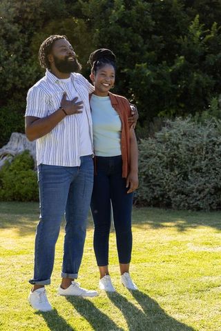 African couple embracing and smiling on sunlit lawn casual park lifestyle portrait