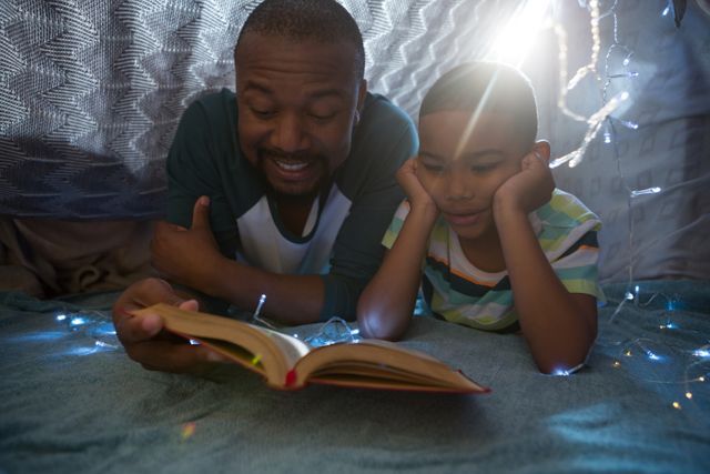 Father and son enjoying a bedtime story together in a cozy bedroom setting. Ideal for use in family-oriented content, parenting blogs, educational materials, and advertisements promoting family bonding and literacy.