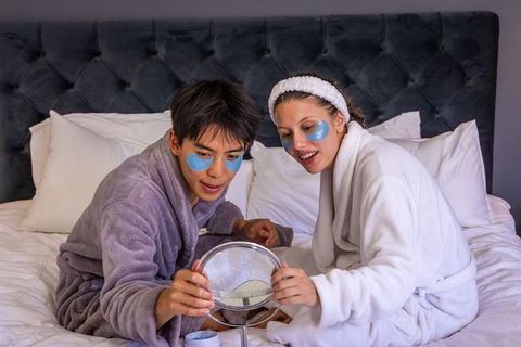 Interracial couple enjoying cozy in-bed skincare routine with under-eye gel patches