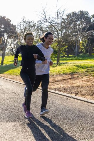 Diverse friends running in park wearing hoodies and fitness tracker