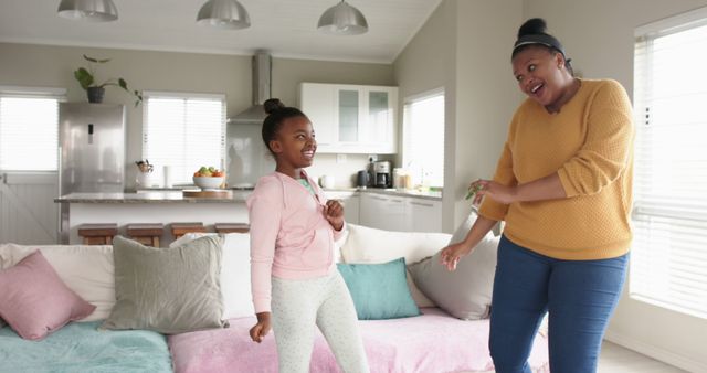 Mother and daughter dancing joyfully in a cozy living room. Ideal for themes like family bonding, parenting, happy moments, home lifestyle, parent-child relationship, and leisure activities.