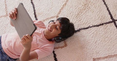 Boy using tablet with headphones on soft rug at home