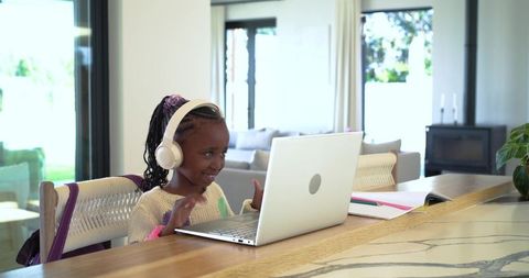 African American Girl Learning Online with Headphones at Home Counter Using Laptop