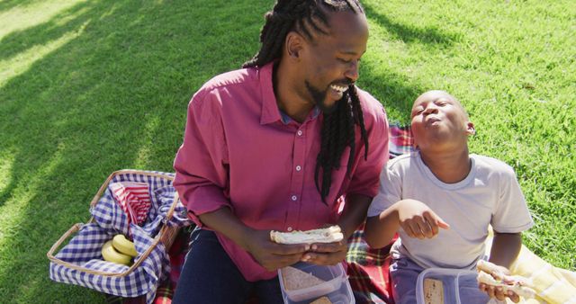 Image of happy african american father and son having picnic outdoors on sunny day. family, togetherness, spending quality time together outdoors.