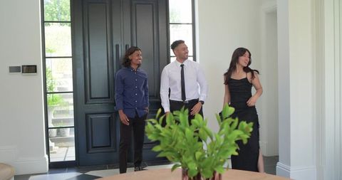 Friends arriving at modern foyer wearing formal attire, smiling and greeting host