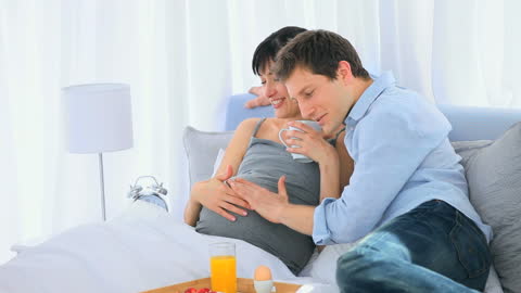 Young Couple Enjoying Breakfast in Bed with Expecting Mother