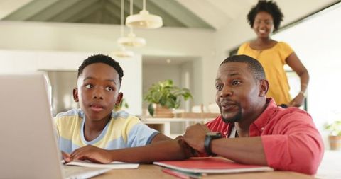 African american father guiding son with laptop homework at bright modern kitchen table