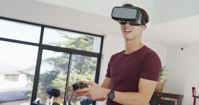Young man wearing VR headset and using a game controller indoors. Perfect for illustrating concepts related to gaming, virtual reality technology, and modern entertainment. Applicable for tech blogs, gaming websites, and advertisements for VR equipment.
