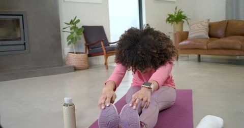 Woman stretching seated forward bend on purple yoga mat wearing smartwatch in pink top