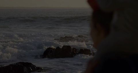 Woman watching waves at dusk on rocky shoreline silhouette conveying coastal solitude