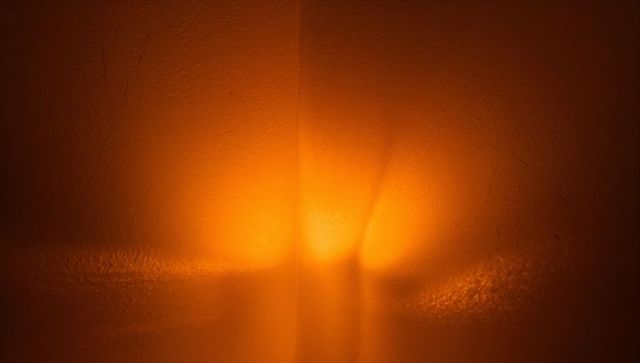 Warm amber glow casting on textured plaster corner with subtle stucco grain