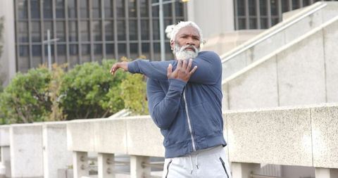 Senior african american man stretching arm outdoors on urban plaza wearing navy hoodie