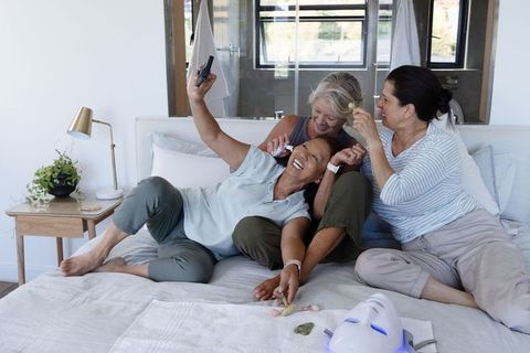 Multigenerational women enjoying at-home skincare spa, taking selfie with led facial gadget